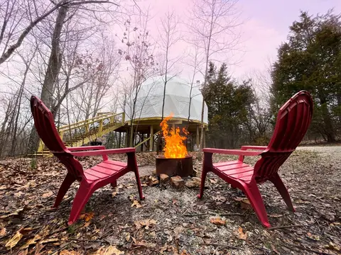 Red Adirondack chairs around the fire pit at sunset, the dome behind